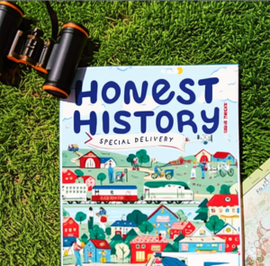A print copy of Honest History magazine lies on a patch of grass, surrounded by nature-themed items. The cover reads “Special Delivery” and features a whimsical, illustrated town scene with trains, bicycles, and busy buildings. Binoculars sit to the left of the magazine, and part of a vintage-style map peeks in from the right, adding to the sense of adventure and exploration.