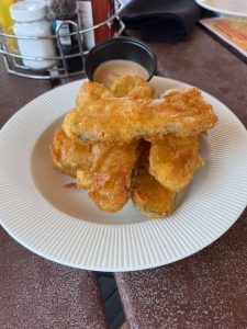 Gluten-free fried pickles served on a white plate at North Side Tavern in Denver. The crispy, golden coating crackles with texture, hinting at their flaky, flavorful bite. A side of dipping sauce completes this Celiac-safe comfort food favorite.