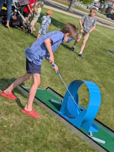 A young boy focused and mid-swing while playing mini golf on the grass during the library’s summer reading kickoff event.