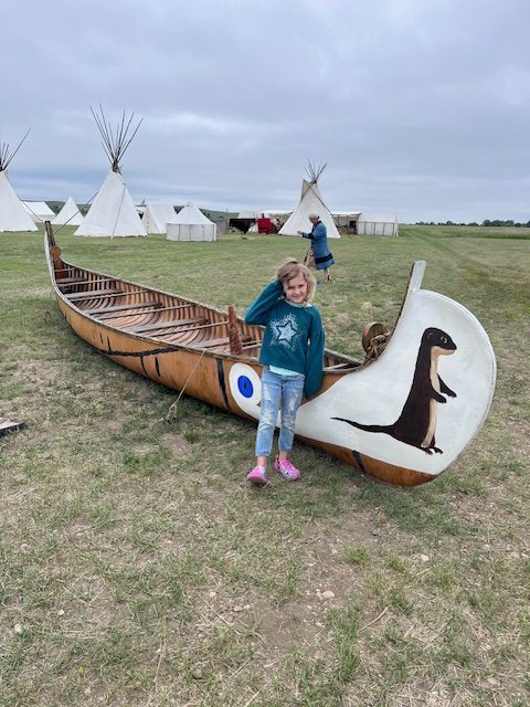 Young girl standing in front of a hand-carved Native American canoe at Fort Union Trading Post during a historical reenactment event.