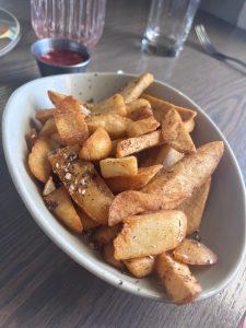 Golden gluten-free fries served in a white bowl at Stanley Marketplace. Lightly seasoned and crisp, the fries are piled high—simple, satisfying, and perfect for sharing on a sunny afternoon.