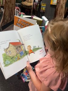 Young girl stands in a cozy children’s bookstore at Stanley Marketplace, intently reading the cover of the humorous book “I Need a New Butt!” Her curious expression and the playful title capture a lighthearted moment of discovery.