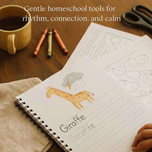 Flat lay of a homeschool table with a spiral-bound workbook open to a giraffe-themed handwriting page, surrounded by crayons, scissors, tea, and printed worksheets.